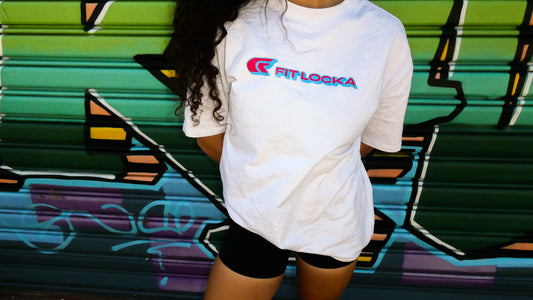 Person wearing a white t-shirt with a fitlocka logo in front of a colorful graffiti wall.